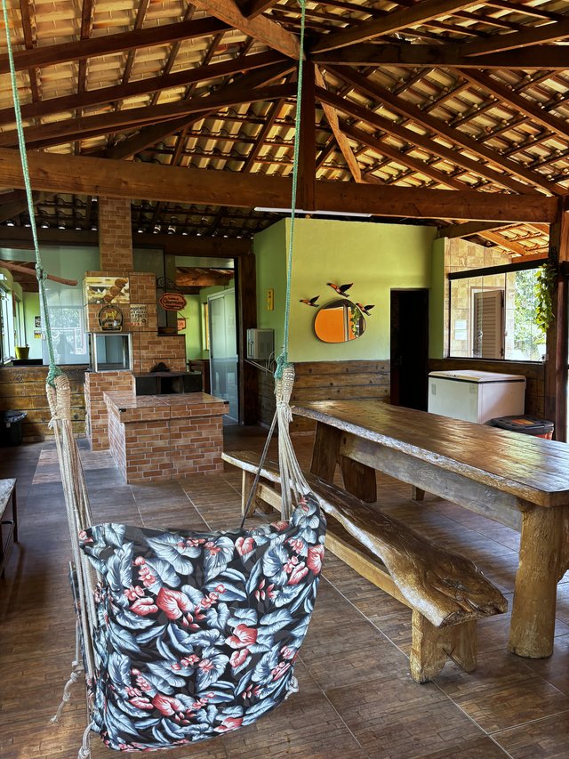 Rancho — Rede suspensa com mesa rústica e churrasqueira ao fundo