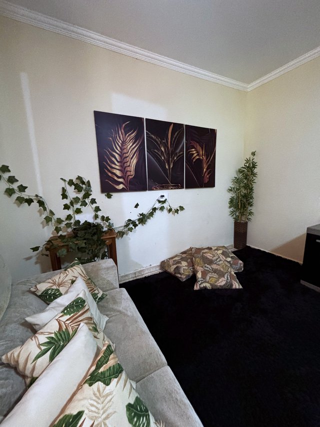 Sala de Estar — Sofá com almofadas tropicais e quadros de folhagens