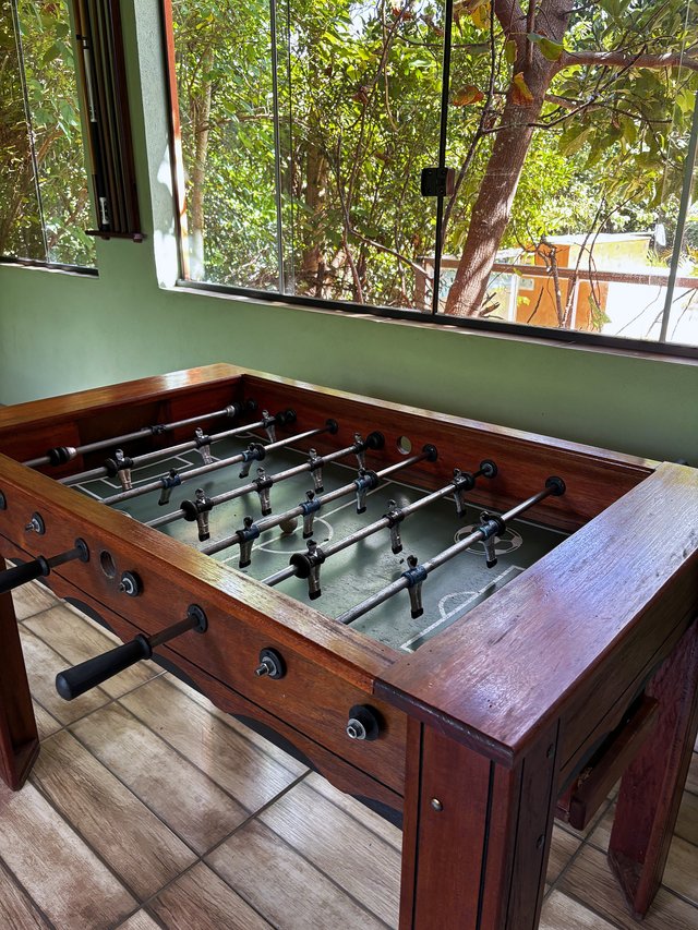 Salão de Jogos — Pebolim de madeira com vista para o jardim pela janela