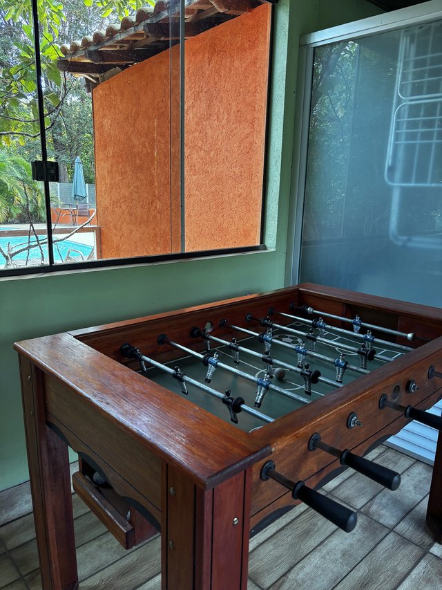 Salão de Jogos — Pebolim com janela aberta para a piscina ao fundo