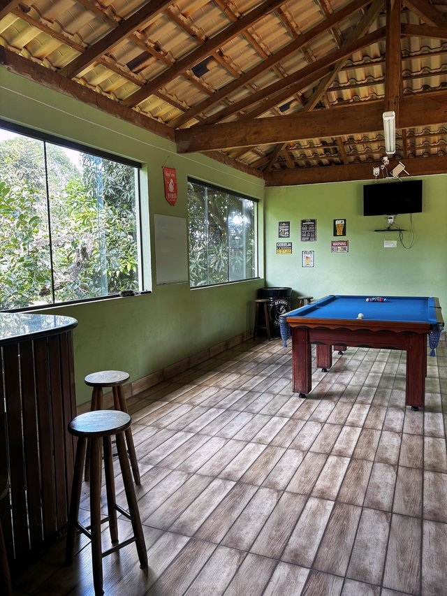 Salão de Jogos — Espaço aberto com mesa de sinuca e janelas para a vegetação