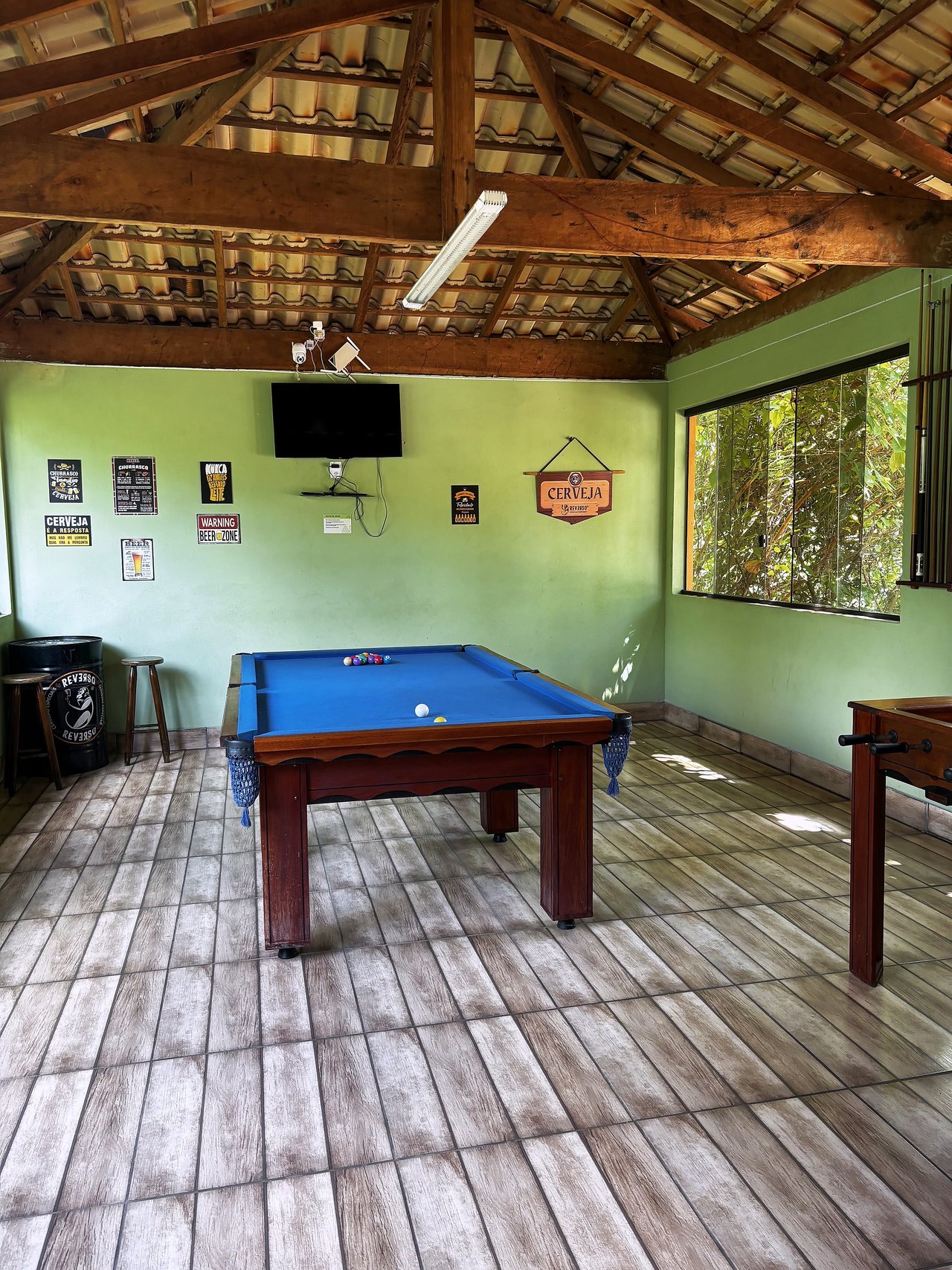 Salão de Jogos — Mesa de sinuca azul com placas decorativas e janela